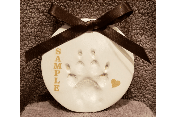 Clay paw print impression from pet, ribbon tied in bow at top of the clay tile.